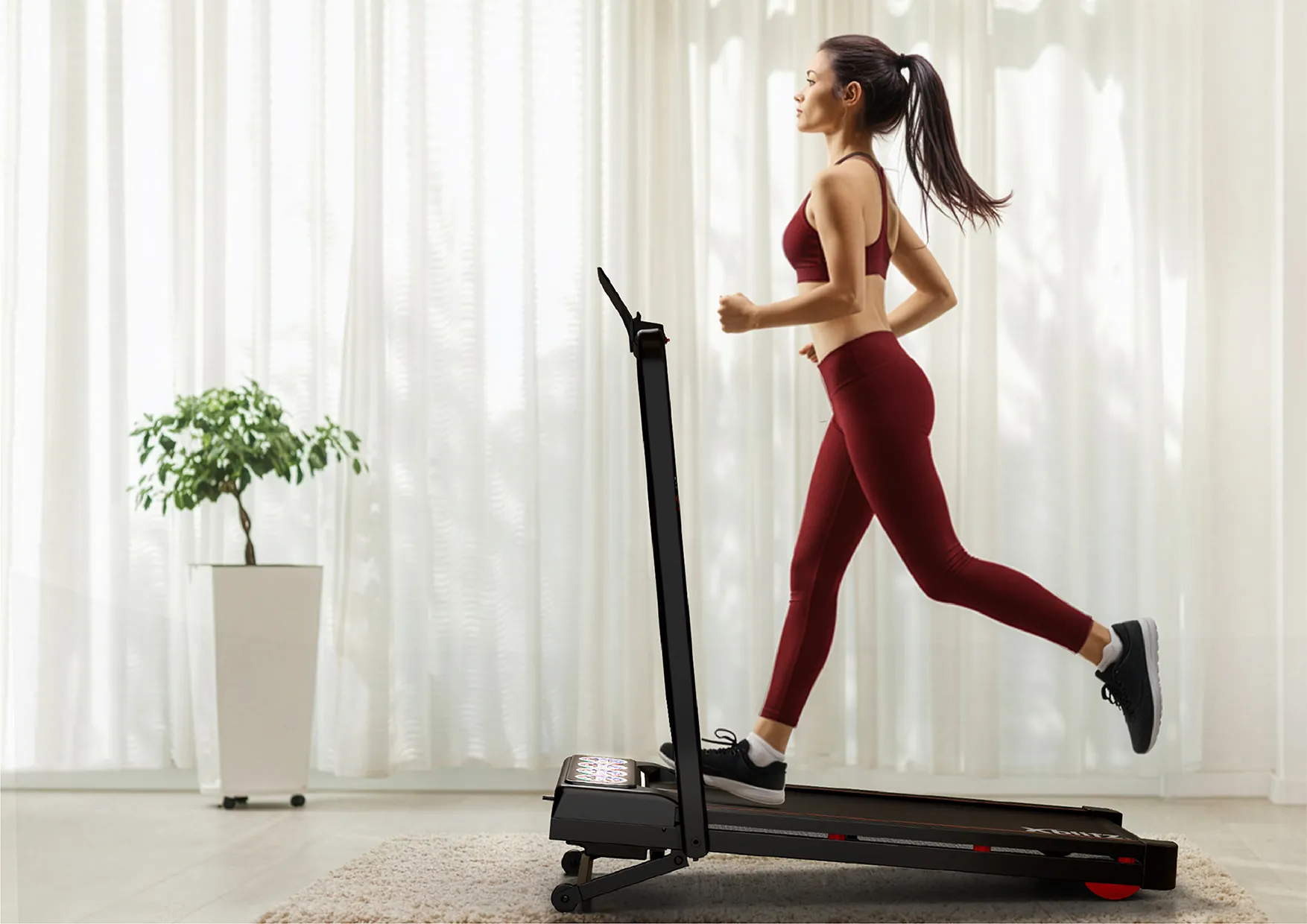 Kobieta w czerwonym stroju sportowym biegnie na bieżni Xblitz Sport X-Runner 2 w jasnym pomieszczeniu z zasłonami